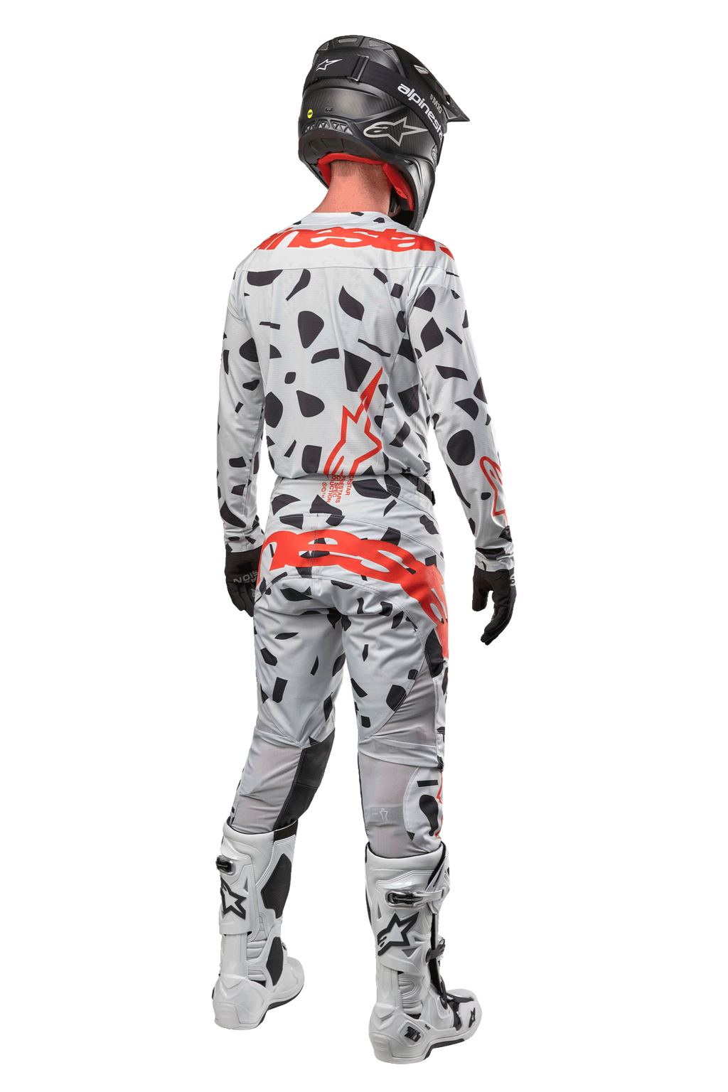 Piloto de motocross desde atrás con pantalones Alpinestars Techstar Rantera 2024, Haze Gray Camo con manchas negras y logotipos rojos, jersey a juego, casco negro y botas blancas, equipamiento completo de carreras todoterreno