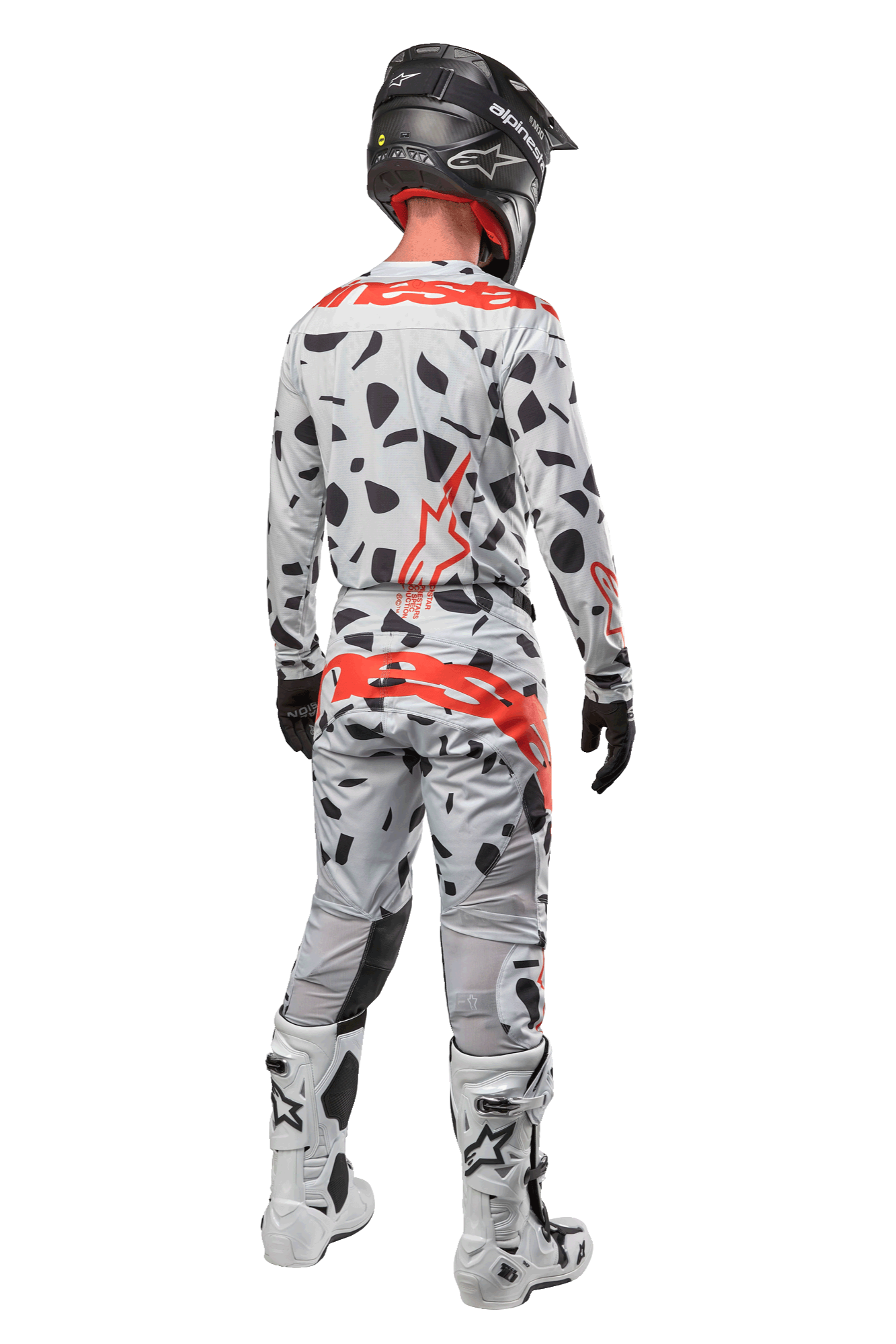 Piloto de motocross desde atrás con pantalones Alpinestars Techstar Rantera 2024, Haze Gray Camo con manchas negras y logotipos rojos, jersey a juego, casco negro y botas blancas, equipamiento completo de carreras todoterreno