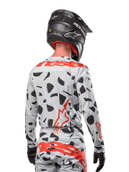 Piloto de motocross desde atrás vistiendo el jersey Alpinestars 2024 Techstar Rantera en Haze Gray Camo, con una base gris claro con manchas gráficas negras y logotipos rojos destacados de Alpinestars en la espalda y hombros, combinado con pantalones a juego y un casco negro.