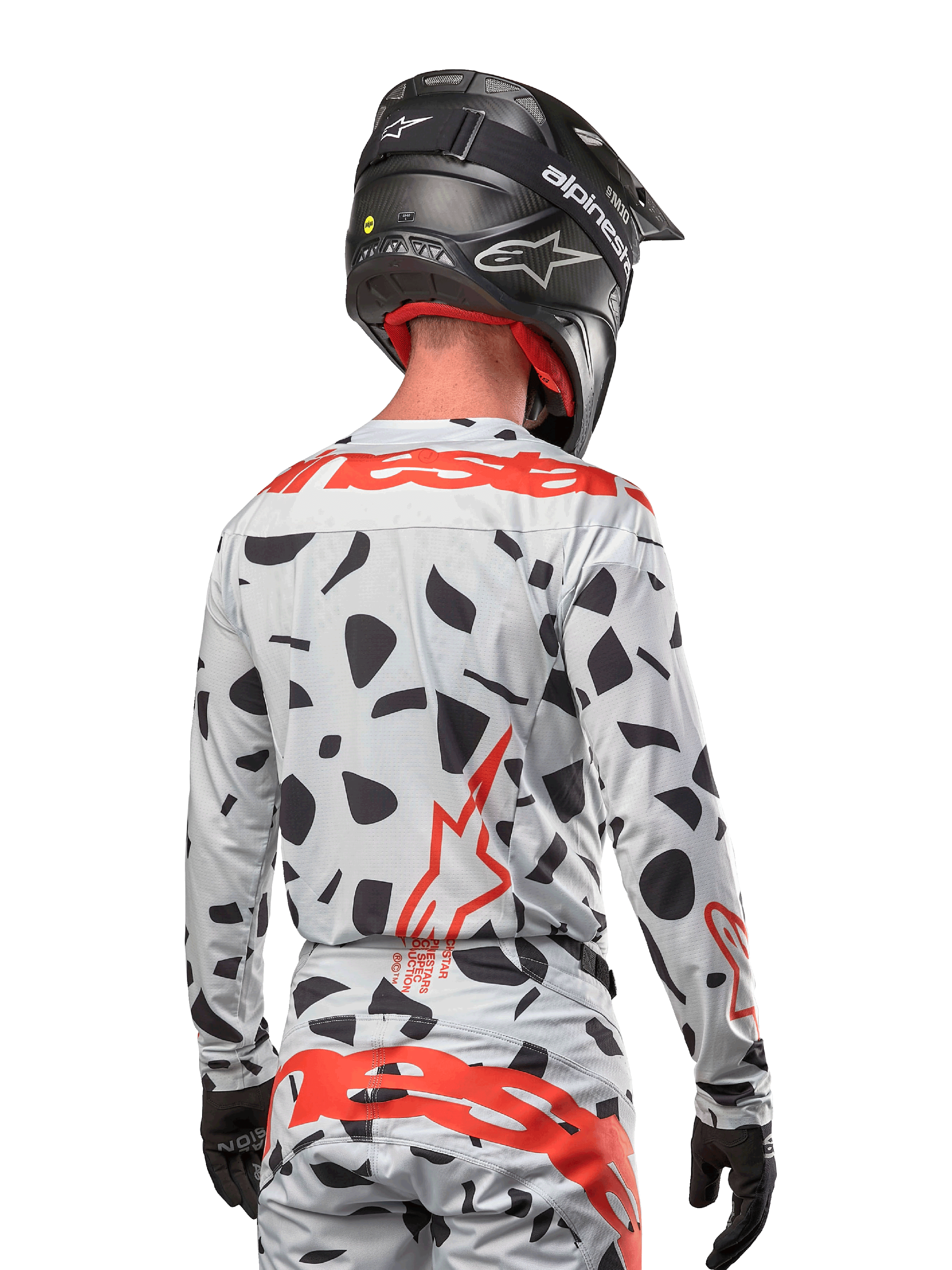 Piloto de motocross desde atrás vistiendo el jersey Alpinestars 2024 Techstar Rantera en Haze Gray Camo, con una base gris claro con manchas gráficas negras y logotipos rojos destacados de Alpinestars en la espalda y hombros, combinado con pantalones a juego y un casco negro.