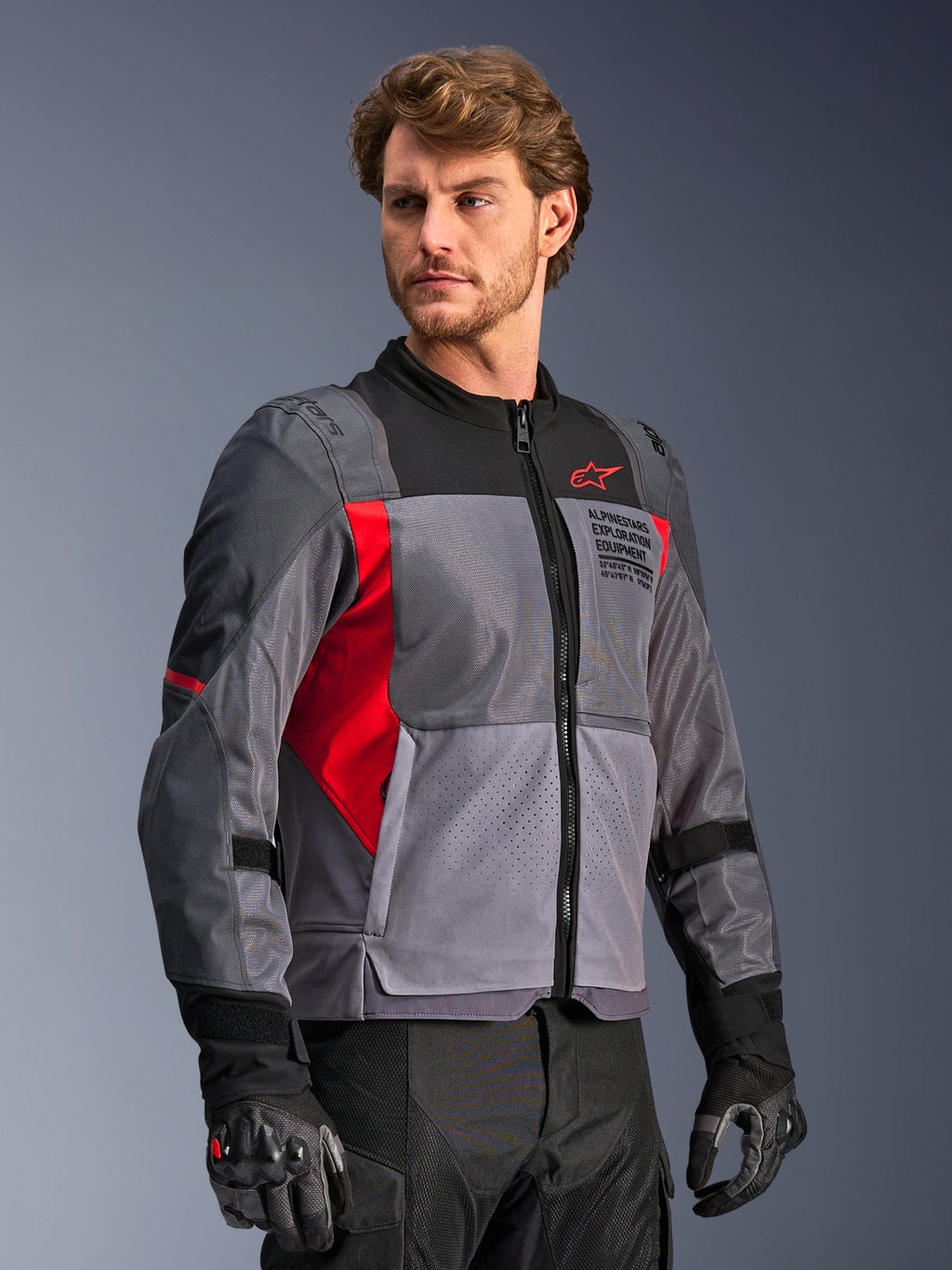 Alpinestars St-2 Air Jacket, Motorcycle Riding Jacket, Deep Gray and Dark Gray with Bright Red accents, featuring large mesh ventilation panels, laser-perforated details, and red star logo, worn by a model in a studio setting, modern adventure touring style