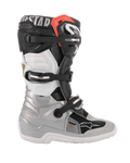 Botas Alpinestars Youth Tech 7S, botas de motocross para jóvenes, color negro, plata, blanco y dorado, vista de perfil lateral con carcasa inferior plateada, paneles superiores en negro y blanco, detalle rojo en el borde superior y sistema de cierre de tres hebillas