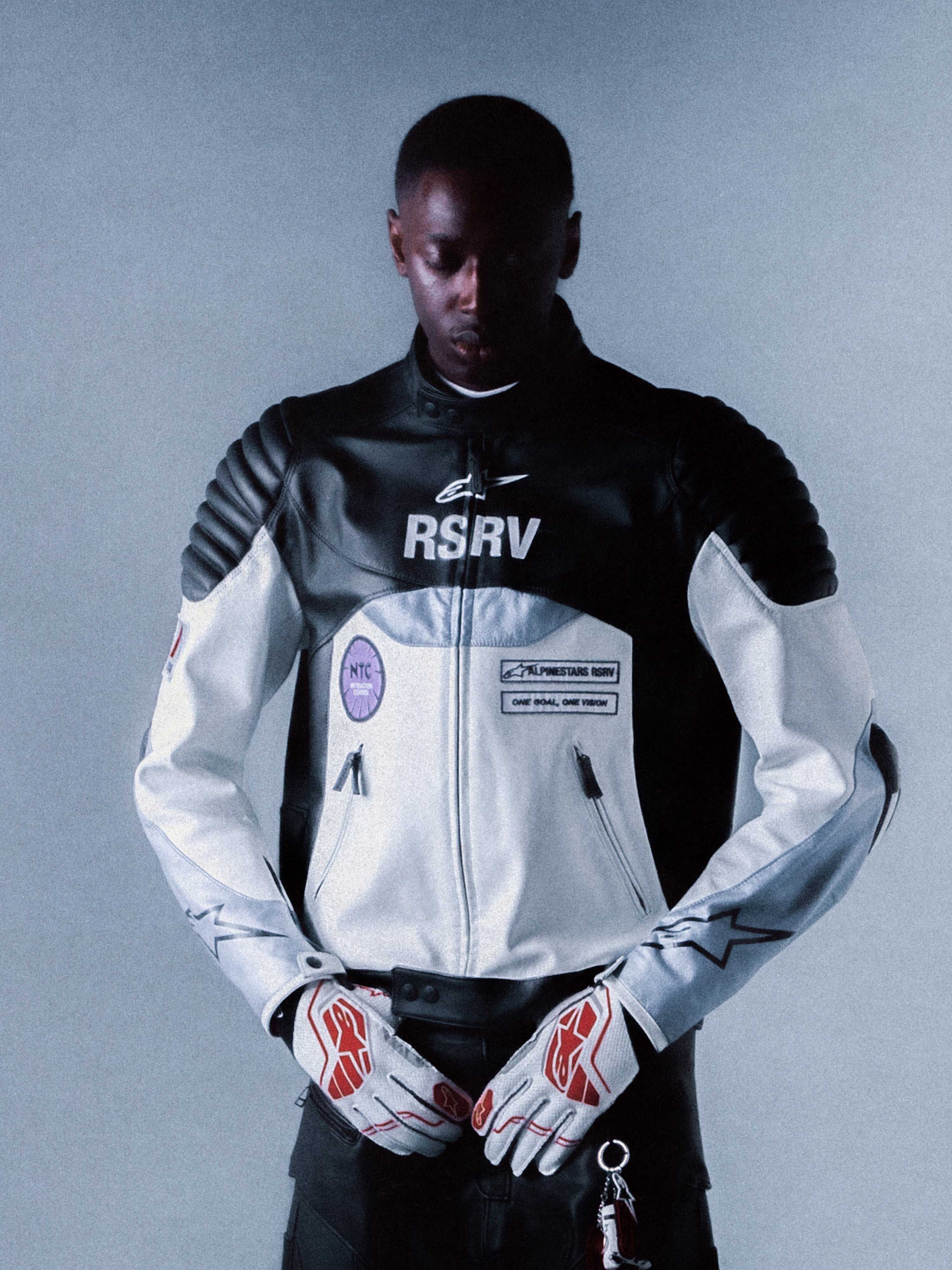 Alpinestars RSRV Threadline Leather Jacket, chaqueta de cuero para moto estilo urbano, negra y blanca, con parches RSRV y hombros acolchados, persona con guantes blancos con detalles rojos, diseño premium de edición limitada